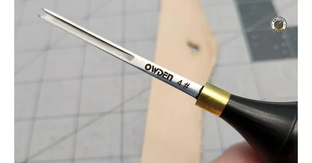 A close-up of an OWDEN pricking iron, a specialized leatherworking awl, resting on a piece of leather on a cutting mat.