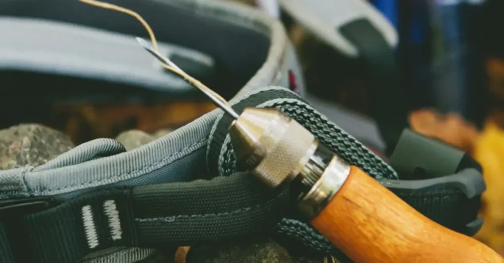 Close-up of a wooden-handled stitching awl being used to sew and repair a heavy-duty nylon strap on a piece of outdoor or camping gear, set against a natural background. What Projects Is the Speedy Stitcher Awl Best For? Outdoor & Leather Fixes